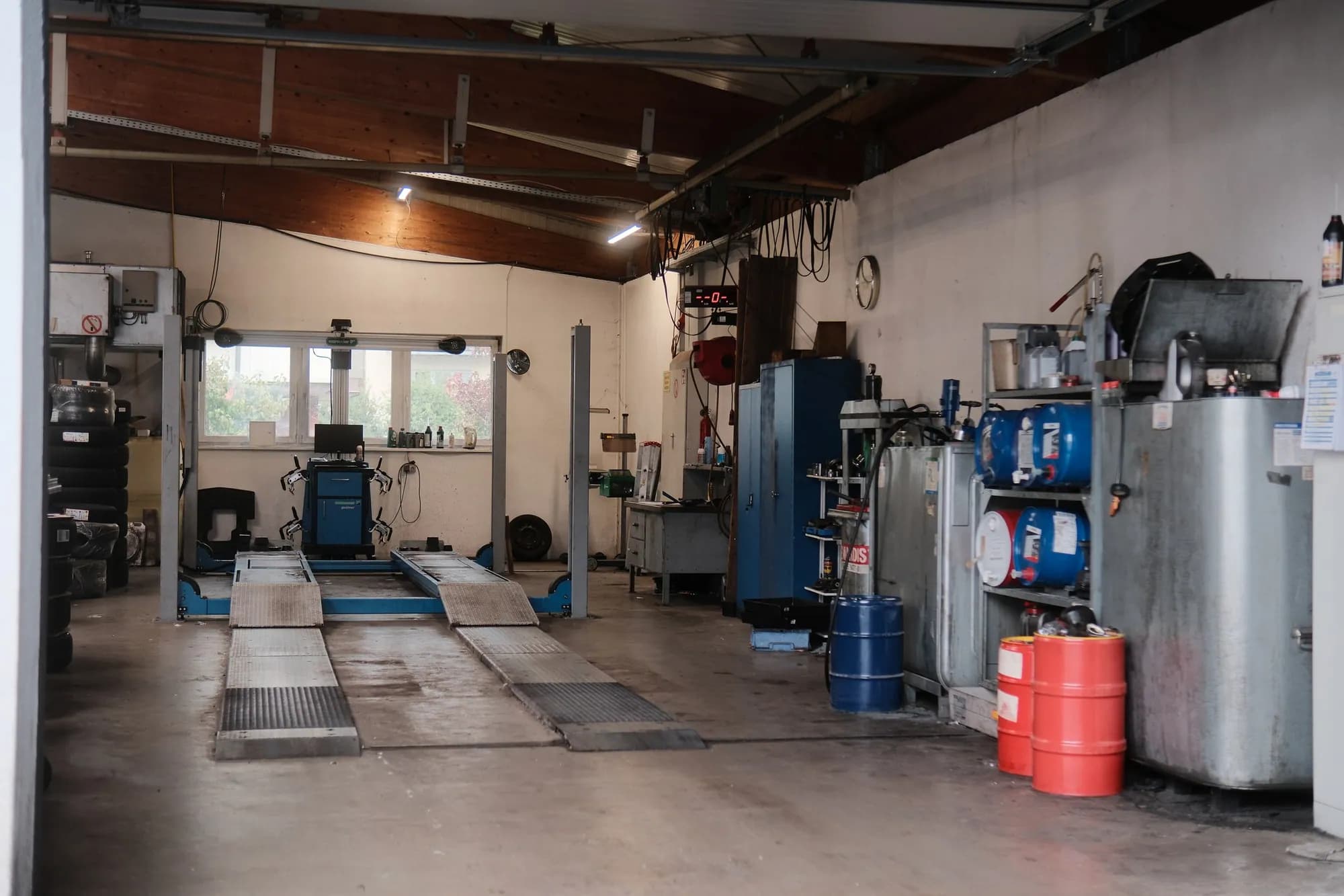 Achsmessplatz in der Halle: die Hebebühne mit zwei Auffahrschienen, an der Stirnwand unter dem Fenster der blaue Achsmesswagen mit Bildschirm und den Messköpfen für die Räder